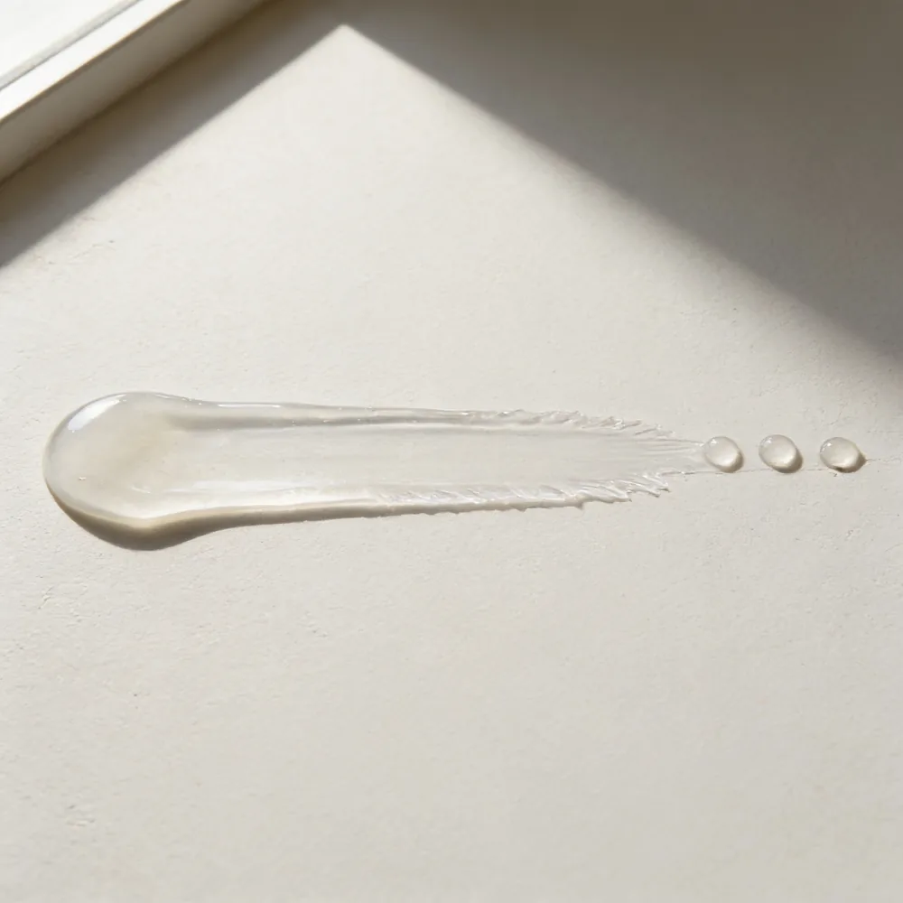 A long flat smear of clear thick gel drawn across a warm off-white surface in low, slanting daylight.