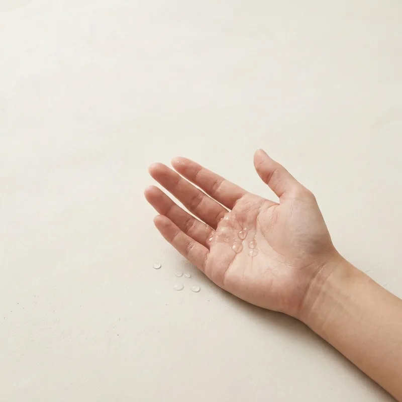 An open palm resting on a warm off-white surface with a few clear drops of the serum in it.