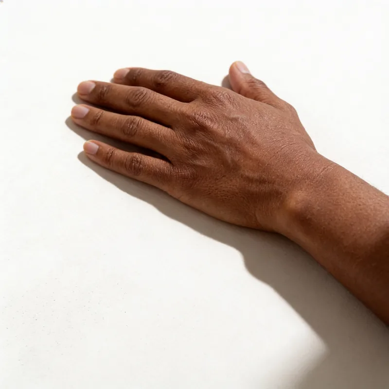 The back of a relaxed hand with deep brown skin resting on a warm off-white surface.