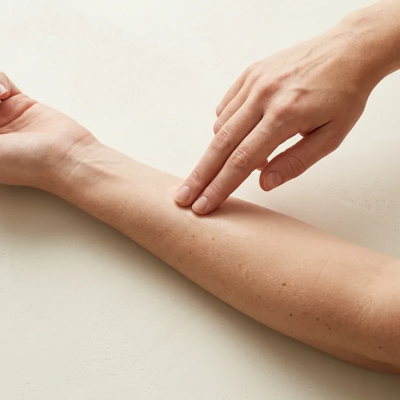 Two fingers pressing the serum into the skin of a forearm.